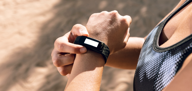 Gros plan d'une femme en tenue de sport utilisant un bracelet connecté pour suivre son activité physique, avec un écran de suivi vierge.
