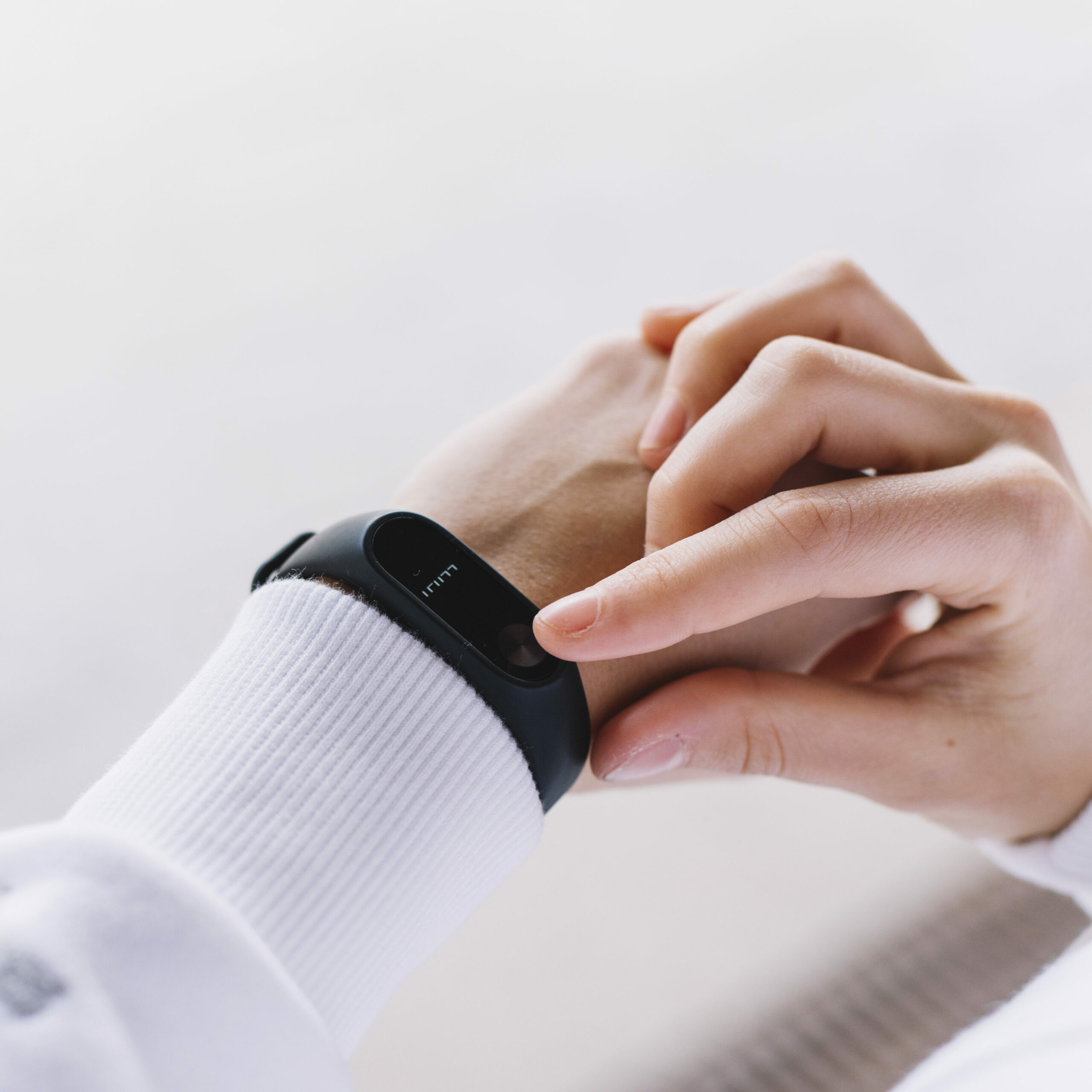 Une personne portant un pull blanc utilise un bracelet connecté noir, en touchant l'écran avec un doigt.