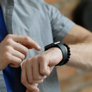 Homme en chemise grise interagissant avec une montre connectée au poignet, représentant la synchronisation d'une smartwatch avec une application. avec des offre promotionelle sur des bracelets connectés de qualité Harmony